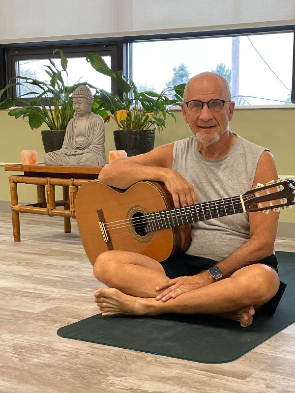 Michael Katz holding a guitar on a yoga mat